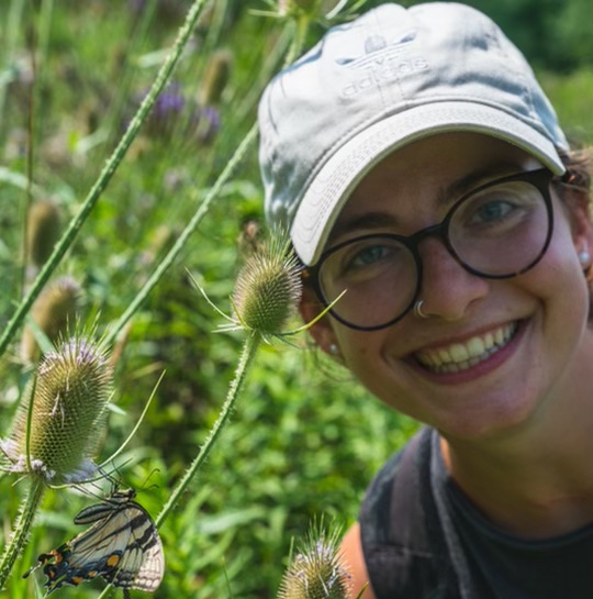 Katie mcManus smiling and posing by a butterfly on a flower