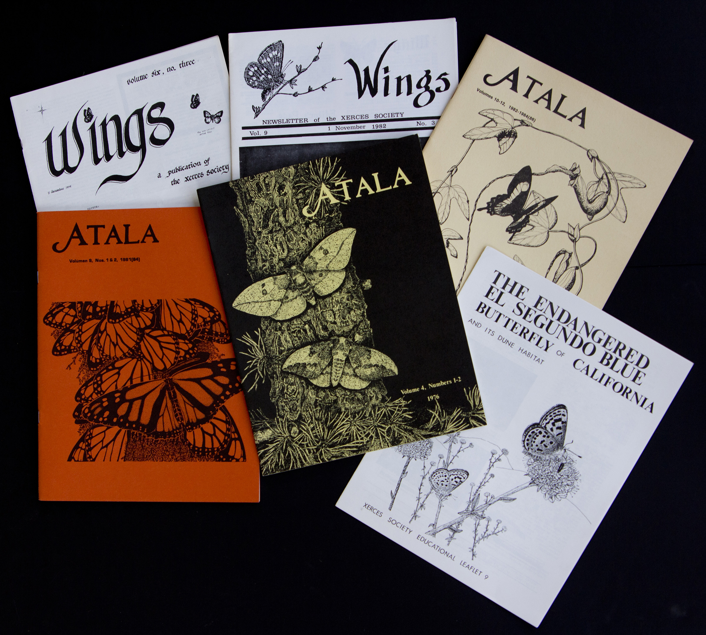 A selection of old publications: Wings newsletter is printed in black-and-white, with the covers of Atala journal are orange, black, and pale yellow.