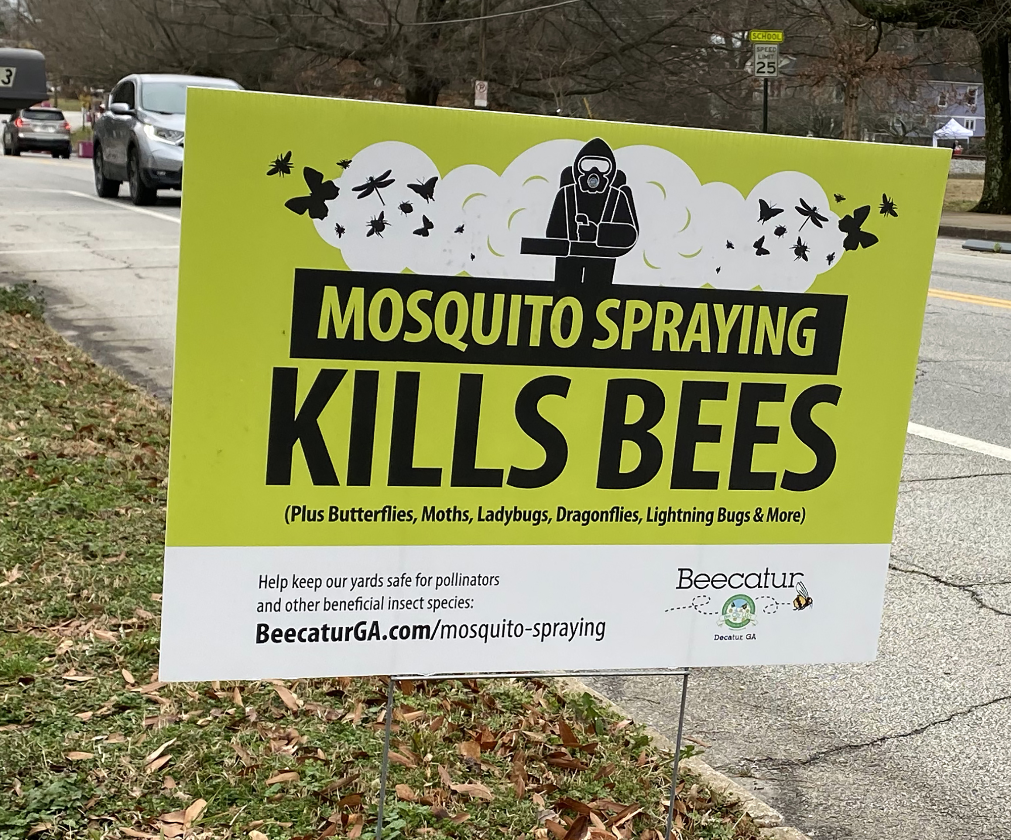 A bright green and white lawn sign declares "mosquito spraying kills bees". Cars drive along the road behind.