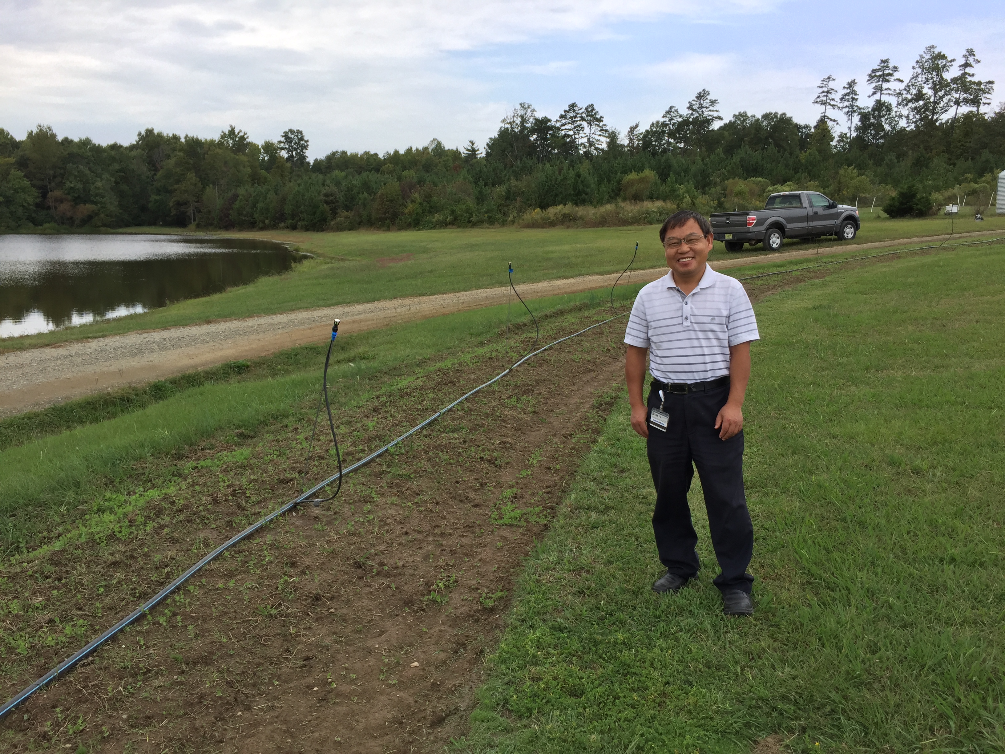 A smiling man stands near the hedgerow-to-be, currently a bed of soil with small plants and some irrigation set up.