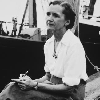 Rachel Carson looks pensive as she sits near a ship, with a book in her lap.