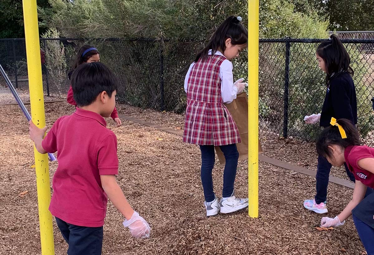 Several students pick up litter on the playground and place it into paper bags