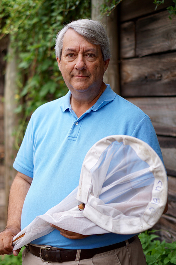 Ted Burk, an older white man with grey hair, holding a butterfly net and smiling.
