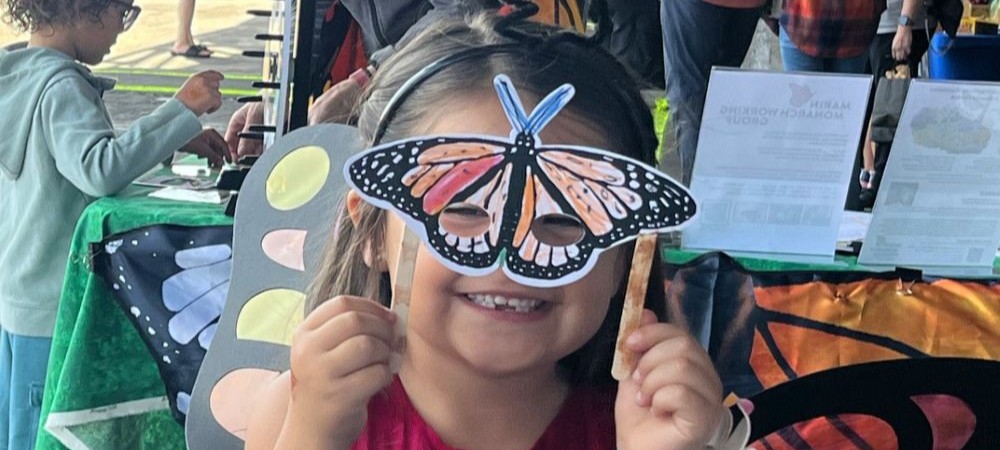A child smiles behind a handmade monarch butterfly max (Photo: Natash Granoff)