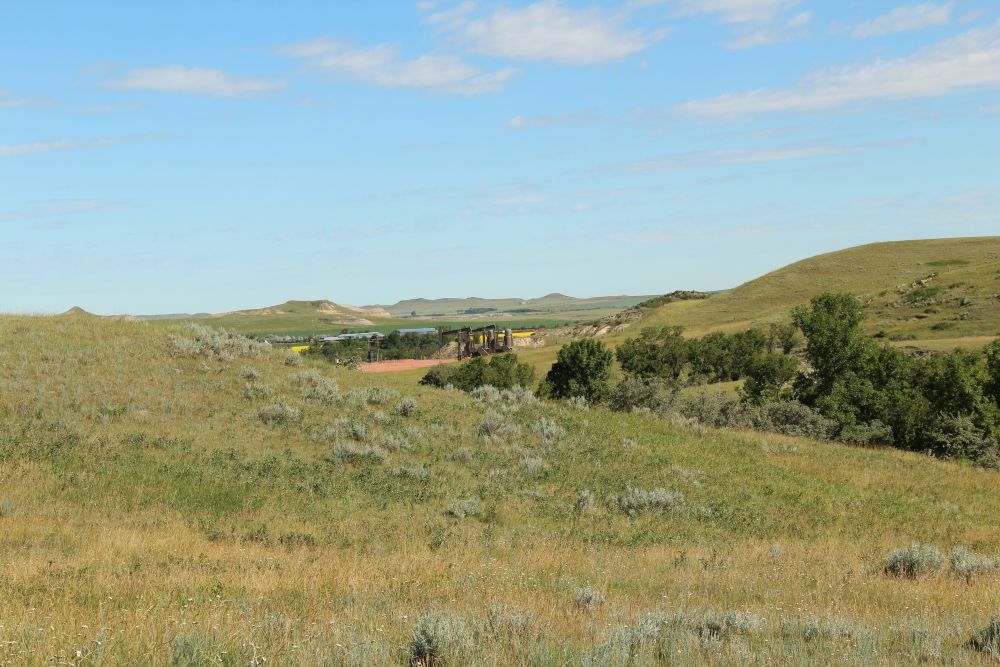 A wide view of a grassland, with crop fields and a set of oil derricks in the middle.