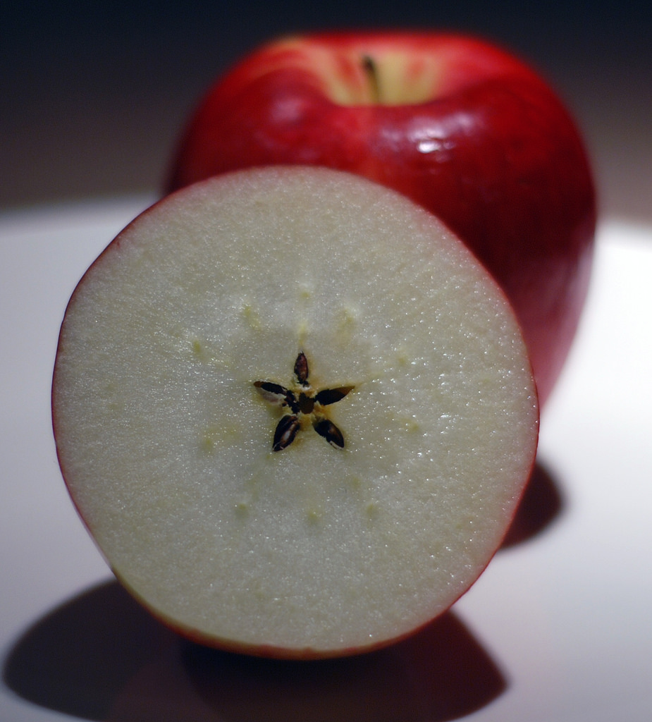 An apple is sliced in half to reveal its star-shaped seed arrangement.