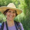 Closeup of a woman smiling in a field, wearing a hat and purple shirt