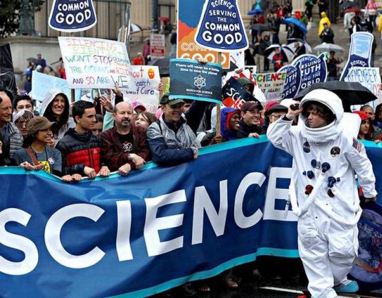 A crowd at a demonstration holds up a banner with the letters "CIENCE" visible across its length.