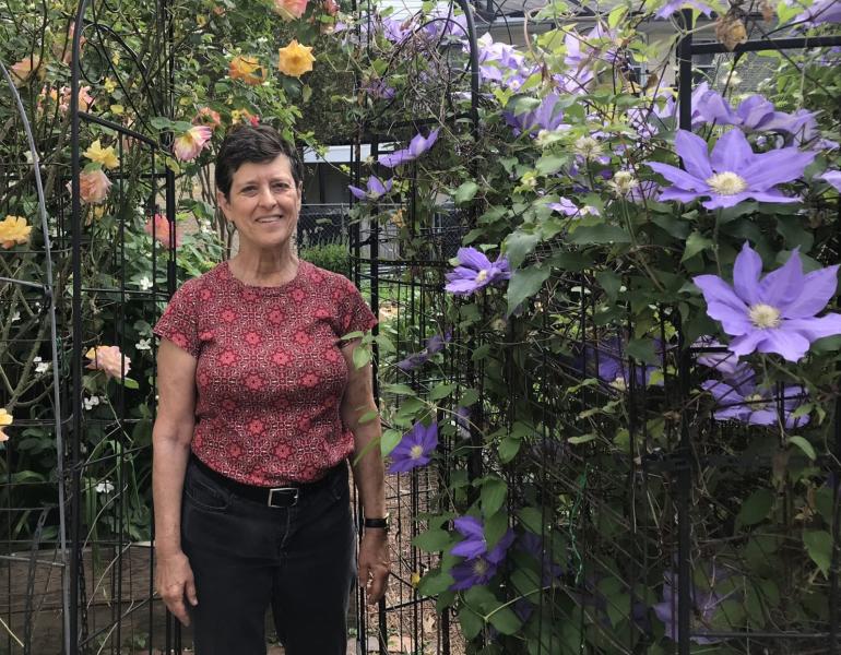 Jan Mooney stands beside purple clematis and yellow rose vines at Upper Fells Point Community Garden. (Photo courtesy of Jan Mooney.)