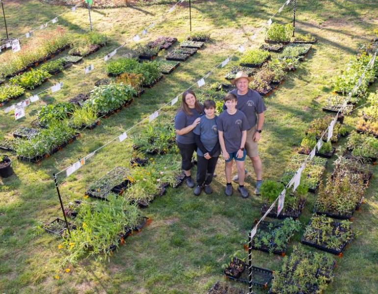 A family of 4 smile surrounded by potted native plant seedlings