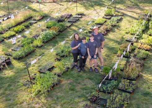 A family of 4 smile surrounded by potted native plant seedlings