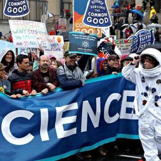 A crowd at a demonstration holds up a banner with the letters "CIENCE" visible across its length.