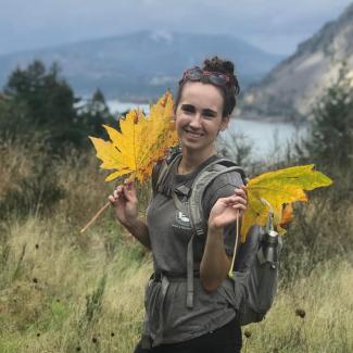 Megan Westby holding up leaves in front of a mountain landscape