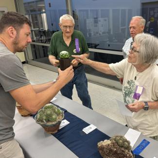 A man holds a potted cactus for 3 judges to view at a plant show and sale