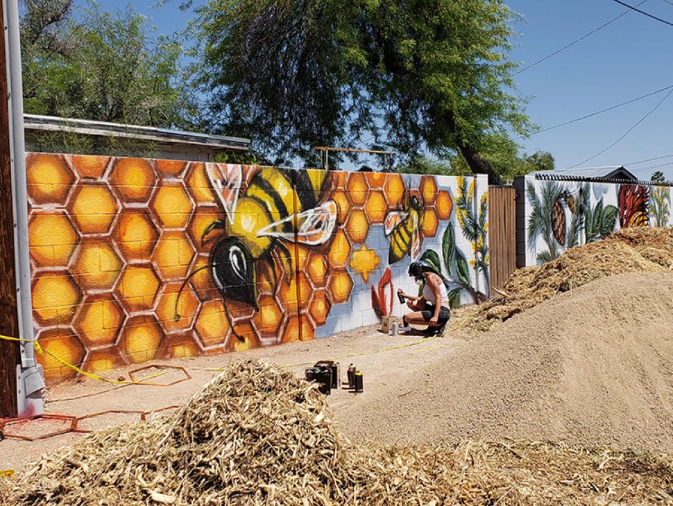 Artist Laura Thurbon painting a wall mural with bee and hexagon motifs 