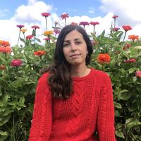 Katherine Price wears a red sweater and sits in front of blooming zinnias